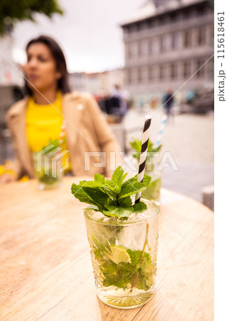 Young woman at a city cafe, sipping a Mojito with modern buildings, creating a trendy atmosphere 115618461