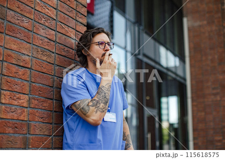 Healthcare worker taking a break, smoking a cigarette outdoors, in front of the hospital building. Healthcare worker taking a break, smoking a cigarette outdoors, in front of the hospital building. 115618575