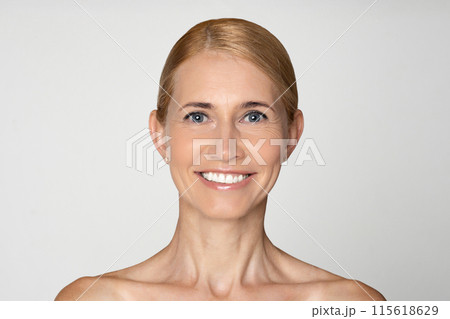 This photo shows a close-up portrait of a middle-aged woman with blonde hair, pulled back from her face, and blue eyes. She has a bright, genuine smile, revealing her white teeth. 115618629