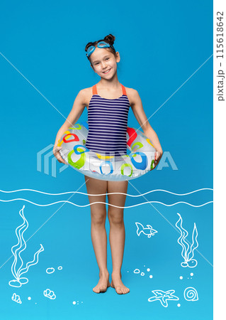 A young girl wearing a bathing suit stands holding an inflatable swimming ring. She is smiling and looks ready to enjoy a swim in the water. 115618642