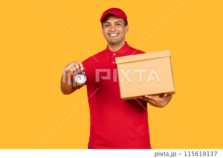 A cheerful delivery man in a red uniform and cap is holding a cardboard box in one hand and an alarm clock in the other. The bright yellow backdrop emphasizes his friendly demeanor and prompt service. A cheerful delivery man in a red uniform and cap is holding a cardboard box in one hand and an alarm clock in the other. The bright yellow backdrop emphasizes his friendly demeanor and prompt service. 115619137