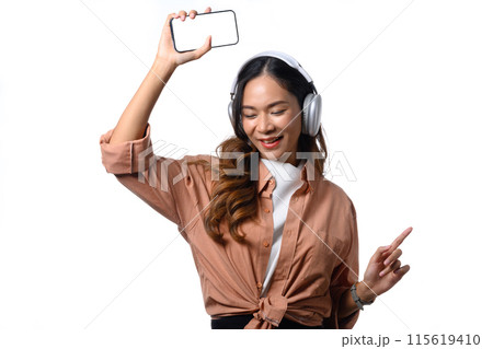 Cheerful young woman listening music with headphones and dancing on white background 115619410