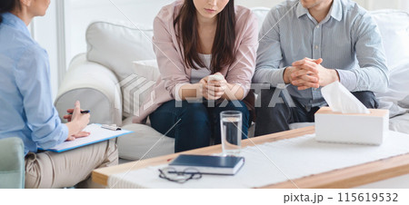 Cropped of couple is seated on a sofa during a counseling session with a therapist. They appear to be engaged in discussion, with the therapist taking notes 115619532