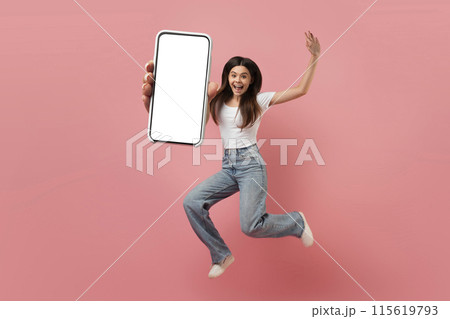 Joyful teen girl jumping in air with big blank smartphone in hand, carefree female teenager demonstrating empty mobile phone, young woman having fun on pink studio background, collage, mockup 115619793