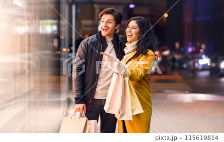 A couple standing in front of a store, holding shopping bags filled with purchases. They look happy and satisfied with their shopping experience. 115619814