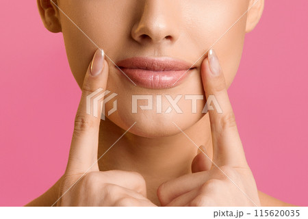 Natural beauty. Young woman applying lip balm, holding fingers near lips, pink background Natural beauty. Young woman applying lip balm, holding fingers near lips, pink background 115620035