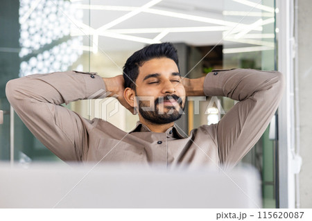 Smiling businessman relaxing with hands behind his head, enjoying a break in a modern office setting. Smiling businessman relaxing with hands behind his head, enjoying a break in a modern office setting. 115620087