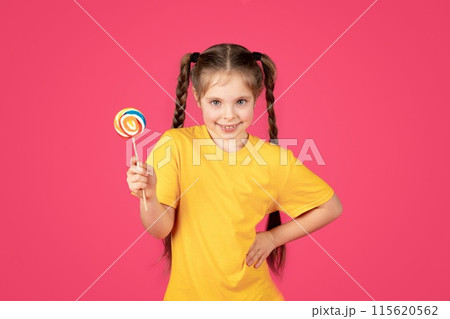 Little Sweet Tooth. Cute preteen girl smiling and holding colorful lollipop, cheerful happy female child with candy in hand looking at camera, posing isolated over pink studio background, copy space 115620562