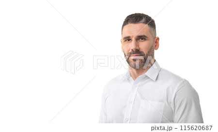 A man with a short beard and trimmed hair is standing against a plain white background, wearing a white button-up shirt. He has a neutral expression, panorama with copy space 115620687