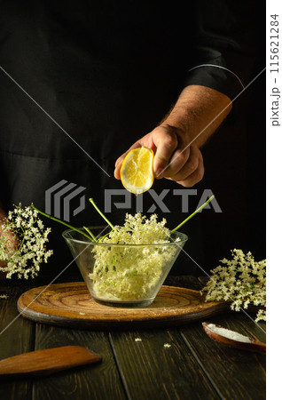 A chef hand squeeze sliced lemon into a bowl of elderflowers before preparing a healthy and tasty drink or kvass on the kitchen table A chef hand squeeze sliced lemon into a bowl of elderflowers before preparing a healthy and tasty drink or kvass on the kitchen table 115621284