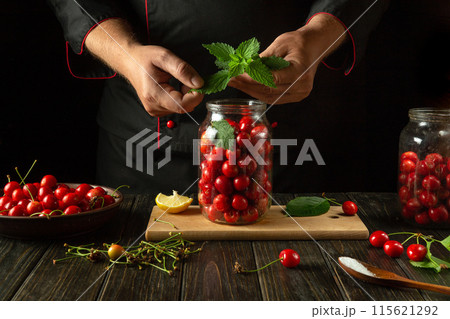 Adding aromatic green mint to a jar of cherries by hand before canning. Concept for making a delicious sweet cherry compote 115621292
