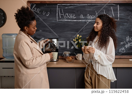 Medium long shot of young smiling multiracial students talking while having coffee break pouring coffee in classroom. Multiethnic millennials enjoying drinks against blackboard 115622458