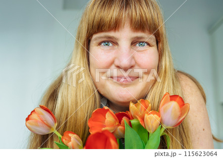 portrait attractive woman with long blond hair, blue eyes, smiling, holding bouquet tulips 115623064