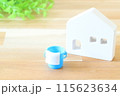 木の板の上にあるミニチュアの白い家とバケツ 115623634