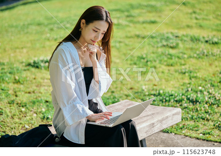 公園でパソコンをタイピングする若い女性 115623748