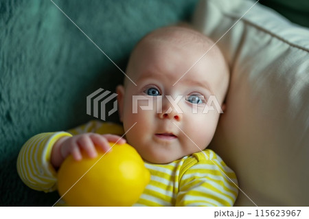 Cute baby with captivating eyes lying down and playing with a bright yellow lemon 115623967