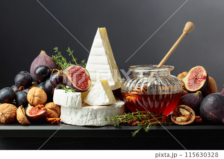Camembert cheese with fruits and honey on a black background. 115630328