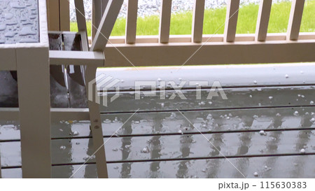 Image capturing a hail storm on a wooden deck, highlighting the impact of hail on patio furniture and the deck surface. Hailstones are visible scattered across the wet deck, with patio furniture in Image capturing a hail storm on a wooden deck, highlighting the impact of hail on patio furniture and the deck surface. Hailstones are visible scattered across the wet deck, with patio furniture in 115630383