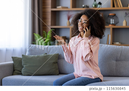 Smiling woman with curly hair having a pleasant phone conversation while sitting on a couch in a cozy living room. 115630845