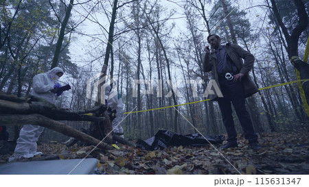 Investigation team examines a murder scene in the forest, focusing on crime evidence collection Investigation team examines a murder scene in the forest, focusing on crime evidence collection 115631347