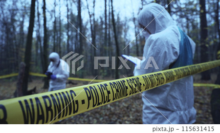 Forensic analysts work at a crime scene secured by tape, focusing on evidence collection Forensic analysts work at a crime scene secured by tape, focusing on evidence collection 115631415