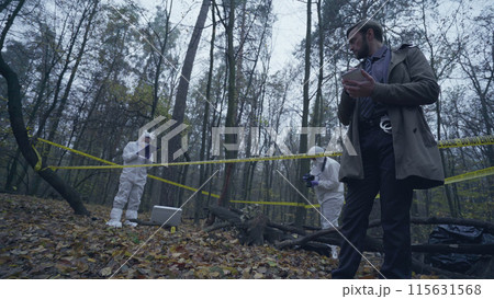 Police detective taking notes at a forest crime scene marked with yellow tape Police detective taking notes at a forest crime scene marked with yellow tape 115631568