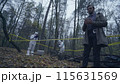 Forensic experts working with evidence in a forest, detective taking notes about the crime scene 115631569