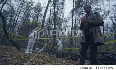Forensic experts working with evidence in a forest, detective taking notes about the crime scene Forensic experts working with evidence in a forest, detective taking notes about the crime scene 115631569