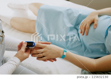 Nurse holding pregnant patients hand and examining her saturation with help of pulse oximeter Nurse holding pregnant patients hand and examining her saturation with help of pulse oximeter 115632130