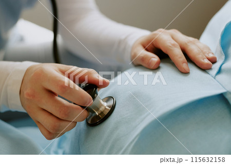 Medium close up of doctors hand holding stethoscope and touching pregnant belly while she listening to unborn babys heartbeat Medium close up of doctors hand holding stethoscope and touching pregnant belly while she listening to unborn babys heartbeat 115632158