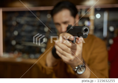Male client choosing handgun in weapon shop, closeup view on gunpoint Male client choosing handgun in weapon shop, closeup view on gunpoint 115632255