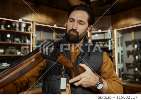 Concentrated salesman checking gun firearm while working at weapon shop 115632317