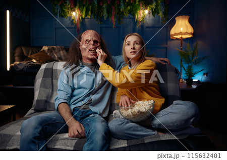 Woman and man wearing monster masks watching movie with popcorn together Woman and man wearing monster masks watching movie with popcorn together 115632401
