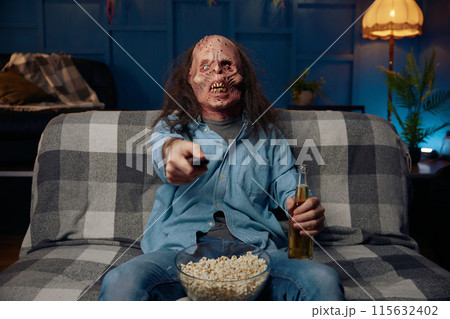 Man wearing zombie mask watching movie with popcorn Man wearing zombie mask watching movie with popcorn 115632402