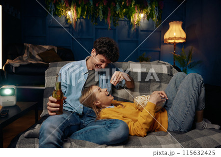 A couple sit on a comfortable couch enjoy popcorn and beer A couple sit on a comfortable couch enjoy popcorn and beer 115632425