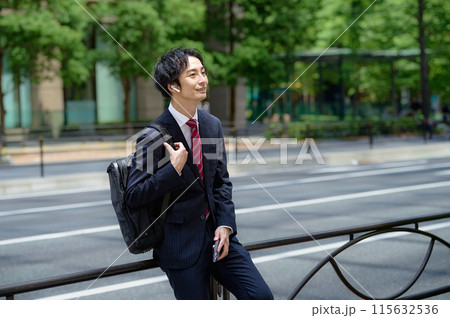スマホを操作するリュックを担いだスーツ姿のビジネスマン スマホを操作するリュックを担いだスーツ姿のビジネスマン 115632536