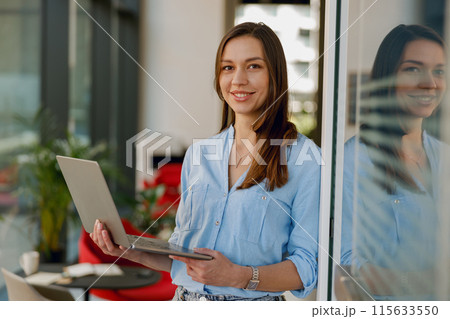 A professional, confident businesswoman smiles while using a laptop in a modern office space A professional, confident businesswoman smiles while using a laptop in a modern office space 115633550