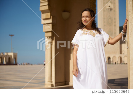 Woman in traditional white dress standing by mosque in the sun Woman in traditional white dress standing by mosque in the sun 115633645