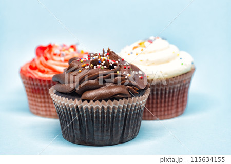 Three cupcakes with colorful sprinkles standing on blue background 115634155