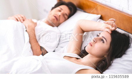 Sleepless young woman staring ceiling while laying next to her snoring partner, have difficulties with sleeping, bedroom interior 115635589