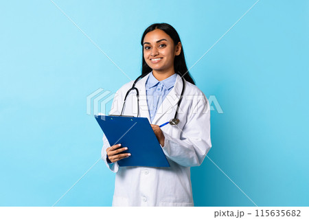 Medical Offer. Confident Young Indian Doctor Lady In White Coat Uniform Posing With Stethoscope And Clipboard, Smiling At Camera, Standing Over Blue Background. Healthcare, General Practitioner Medical Offer. Confident Young Indian Doctor Lady In White Coat Uniform Posing With Stethoscope And Clipboard, Smiling At Camera, Standing Over Blue Background. Healthcare, General Practitioner 115635682