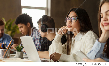 Studying in college library. Thoughtful girl using laptop, preparing for final exam Studying in college library. Thoughtful girl using laptop, preparing for final exam 115635804