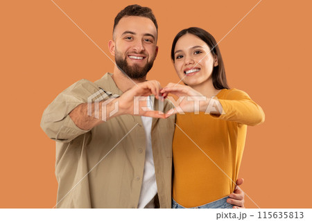 A man and woman are standing close together, forming a heart shape with their hands in front of their chests. They are smiling and looking at each other with joy. A man and woman are standing close together, forming a heart shape with their hands in front of their chests. They are smiling and looking at each other with joy. 115635813