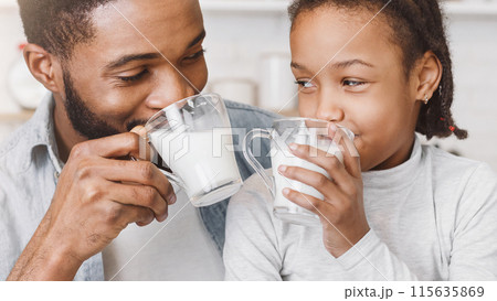 Time for vitamins. Cute Little African Girl And Her Handsome Dad Drinking Milk In Kitchen, watching each other Time for vitamins. Cute Little African Girl And Her Handsome Dad Drinking Milk In Kitchen, watching each other 115635869