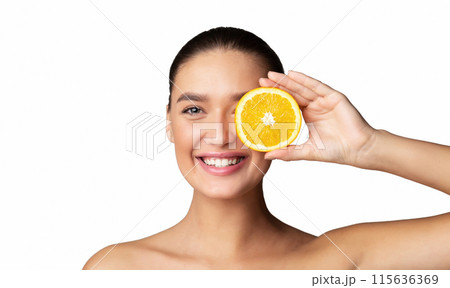 A woman is holding a slice of orange over her face, as if pretending its a smile. Her hand is delicately grasping the bright orange fruit, which contrasts with her skin tone. A woman is holding a slice of orange over her face, as if pretending its a smile. Her hand is delicately grasping the bright orange fruit, which contrasts with her skin tone. 115636369