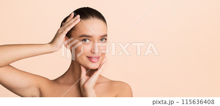 A woman stands with her hands pressed against her cheeks, adding a dramatic effect to her pose. She looks directly at the camera, showcasing a sense of contemplation or surprise. copy space 115636408
