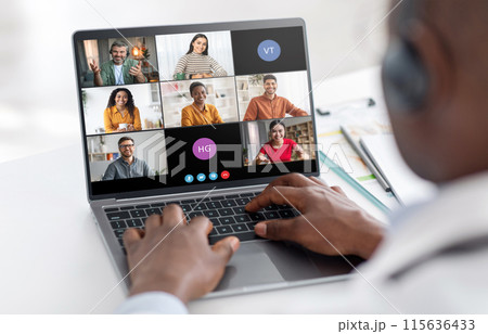 A man sits at a desk, his hands typing on a laptop keyboard, while participating in a video conference. The screen shows six participants in individual video frames. A man sits at a desk, his hands typing on a laptop keyboard, while participating in a video conference. The screen shows six participants in individual video frames. 115636433
