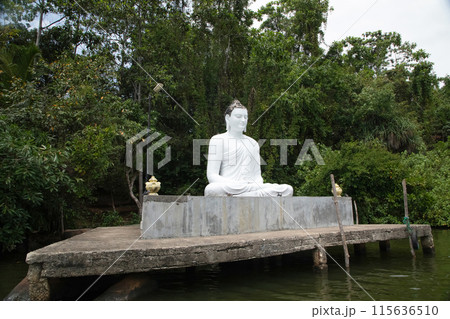 Beruwala,Sri Lanka. 02 february 2023 .white Buddha figure sits over lake. Background beautiful nature palm trees,blue sky. Asia travel and religion concept 115636510