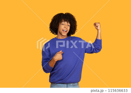 A young man with a dark curly and a big smile stands against a yellow backdrop, flexing his bicep while pointing at himself with his other hand. He appears confident and proud of his strength 115636633