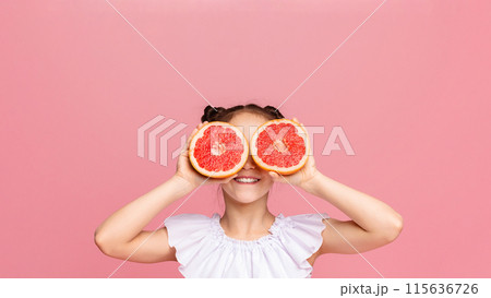 Fruit glasses. Cute girl holding grapefruit slices near her eyes, pink studio background 115636726